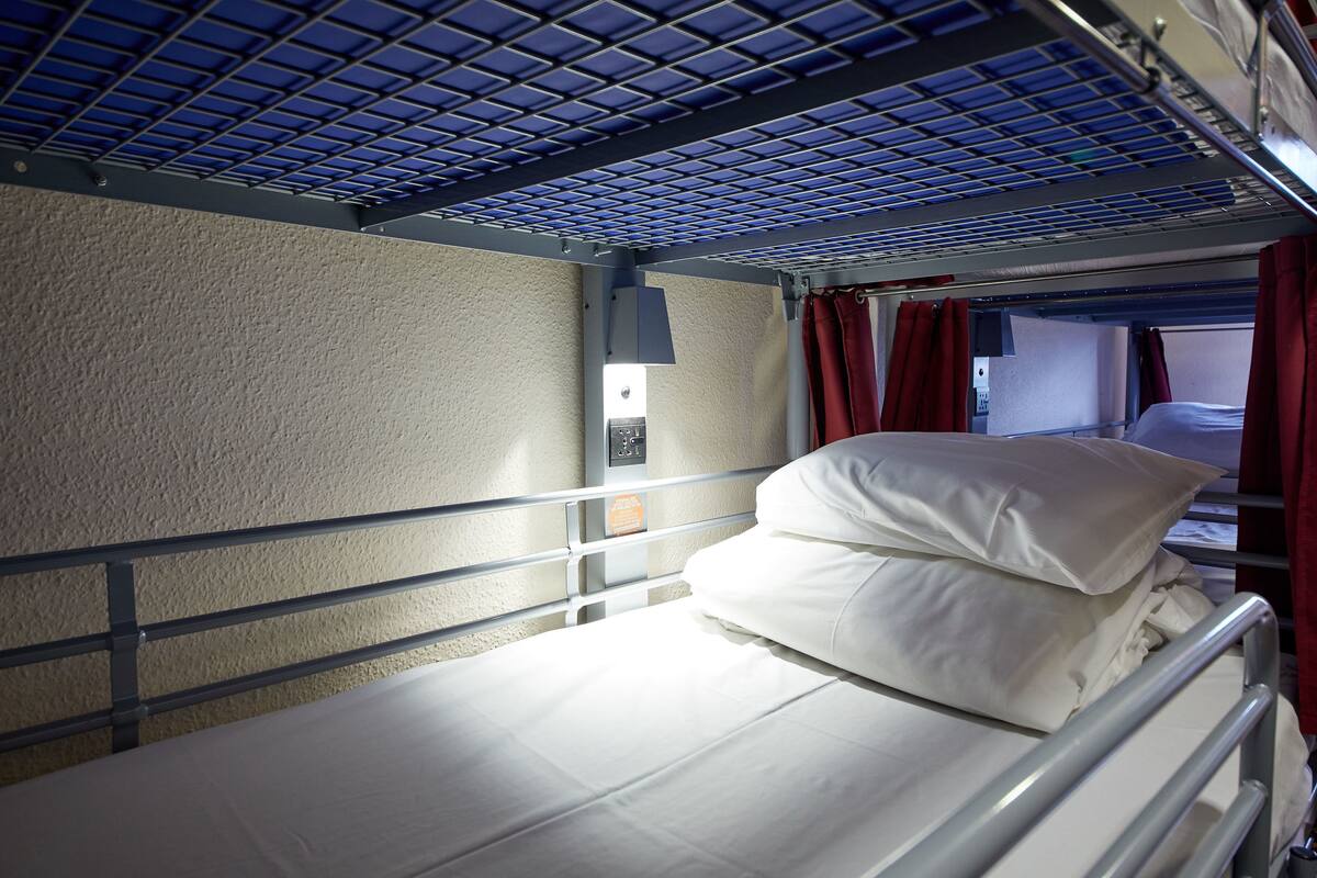 A bunk bed with a metal frame, a white mattress, and red curtains.