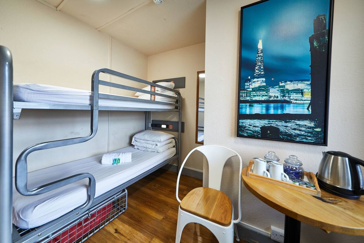 A bunk bed room with a table and chair, a painting of a cityscape, and a kettle on the table.