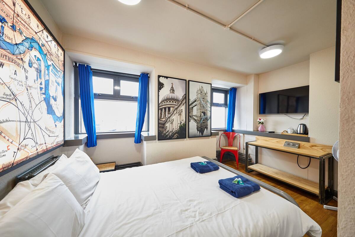 A hotel room with a large bed, a desk with a chair, a flat-screen TV, and a map on the wall.