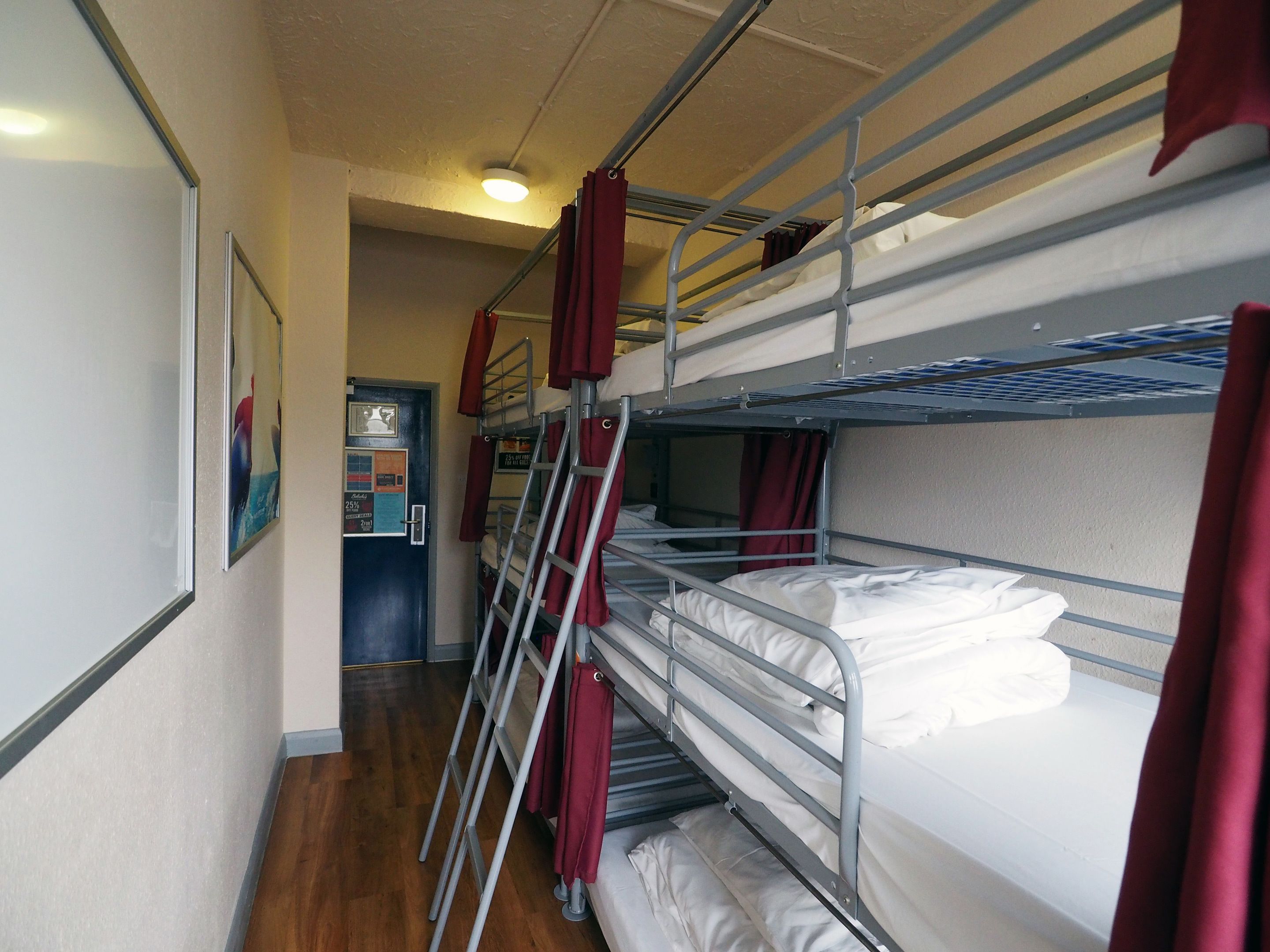 A corridor with bunk beds, a door with a poster, and a ceiling light.