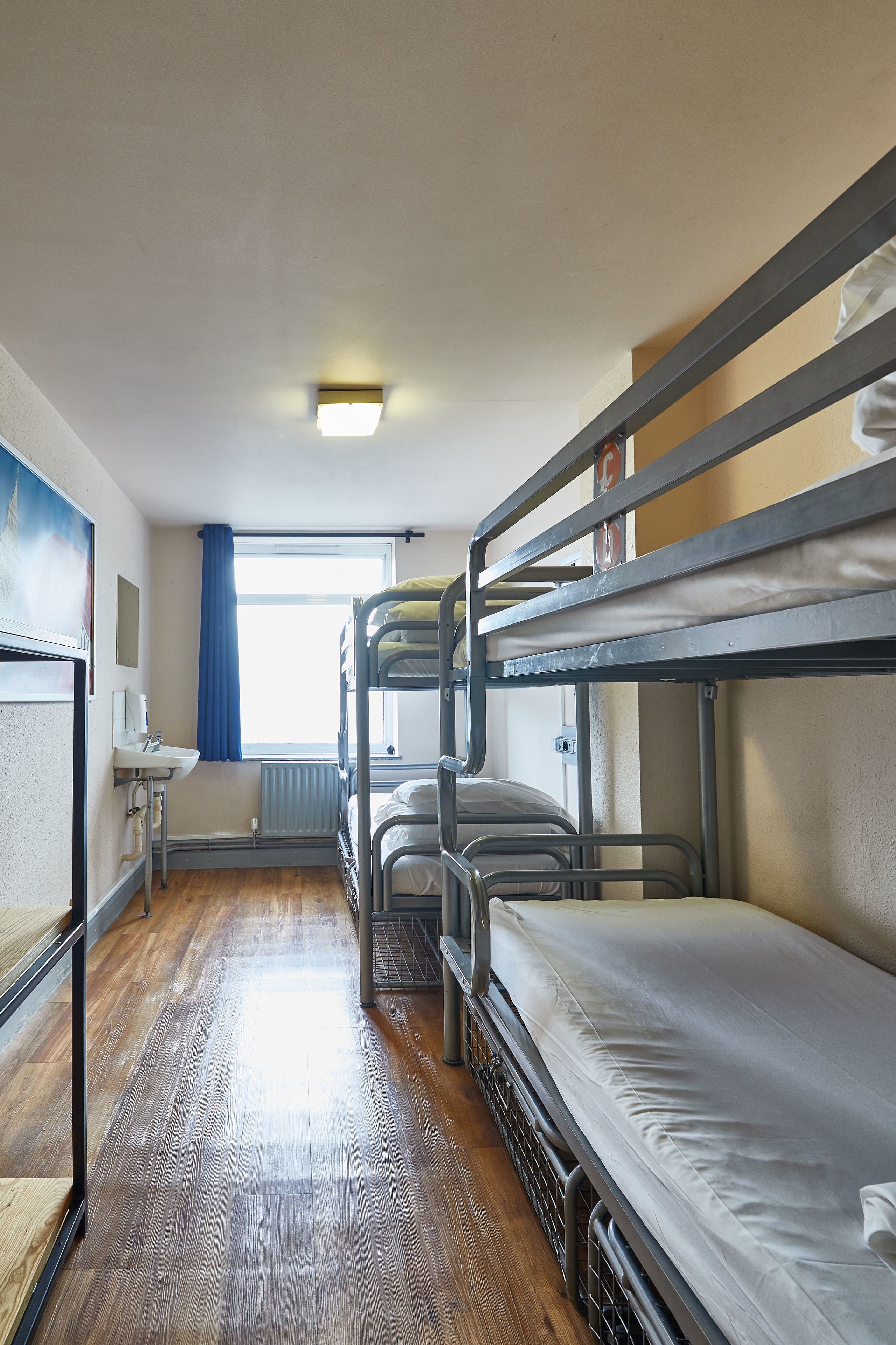 A bunk room with bunk beds, a sink, and a window with blue curtains.