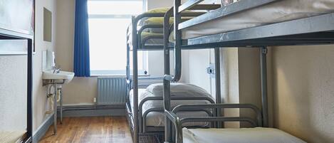 A bunk room with bunk beds, a sink, and a window with blue curtains.