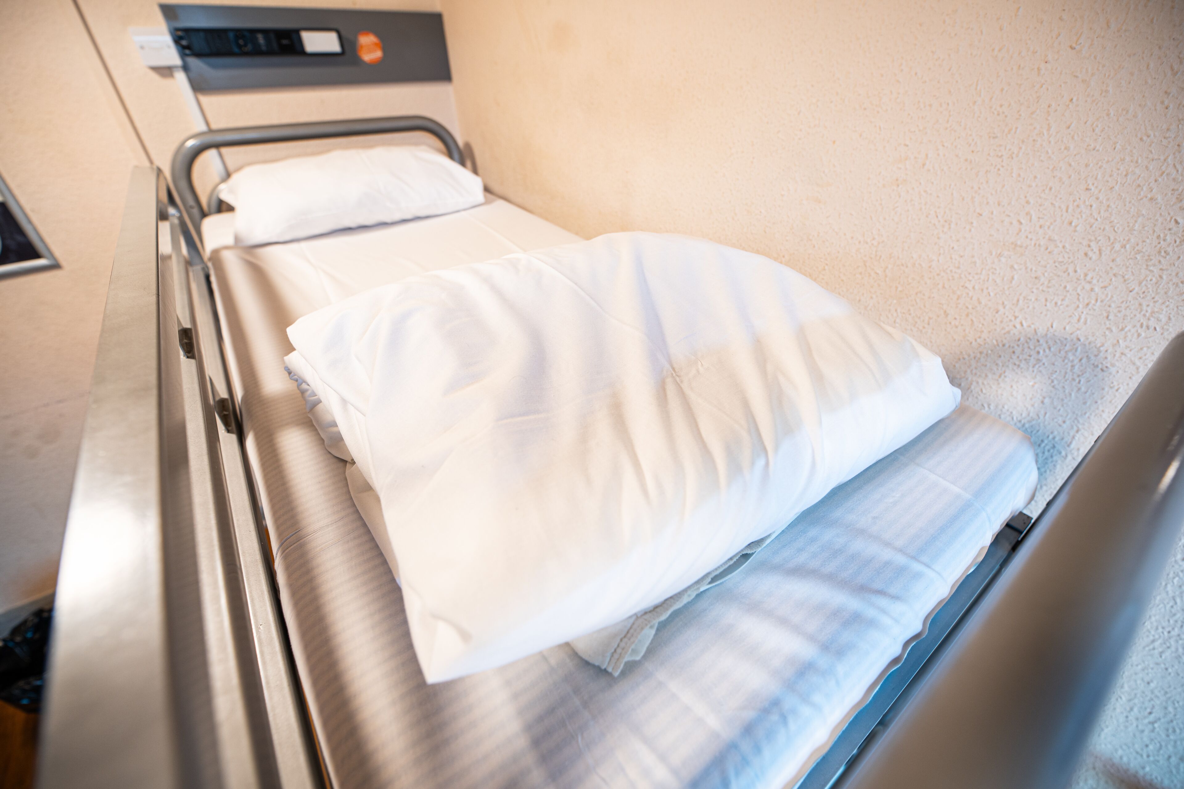 A hospital bed with white linens and a headboard.