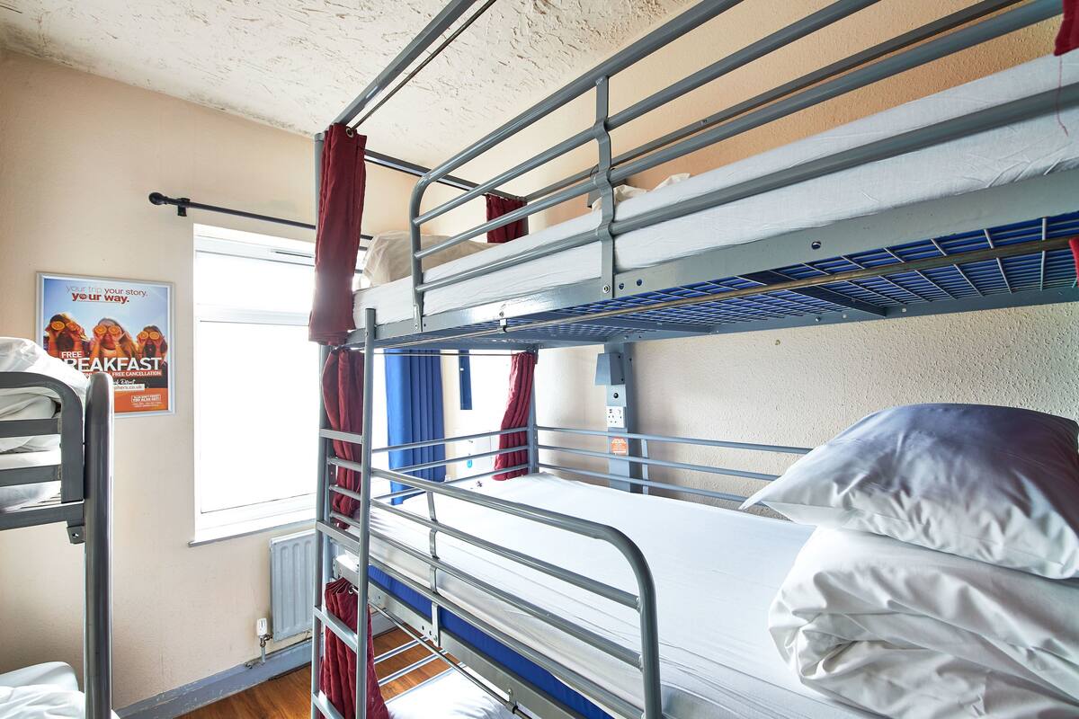 A bunk bed room with a poster on the wall, a window with curtains, and a radiator.