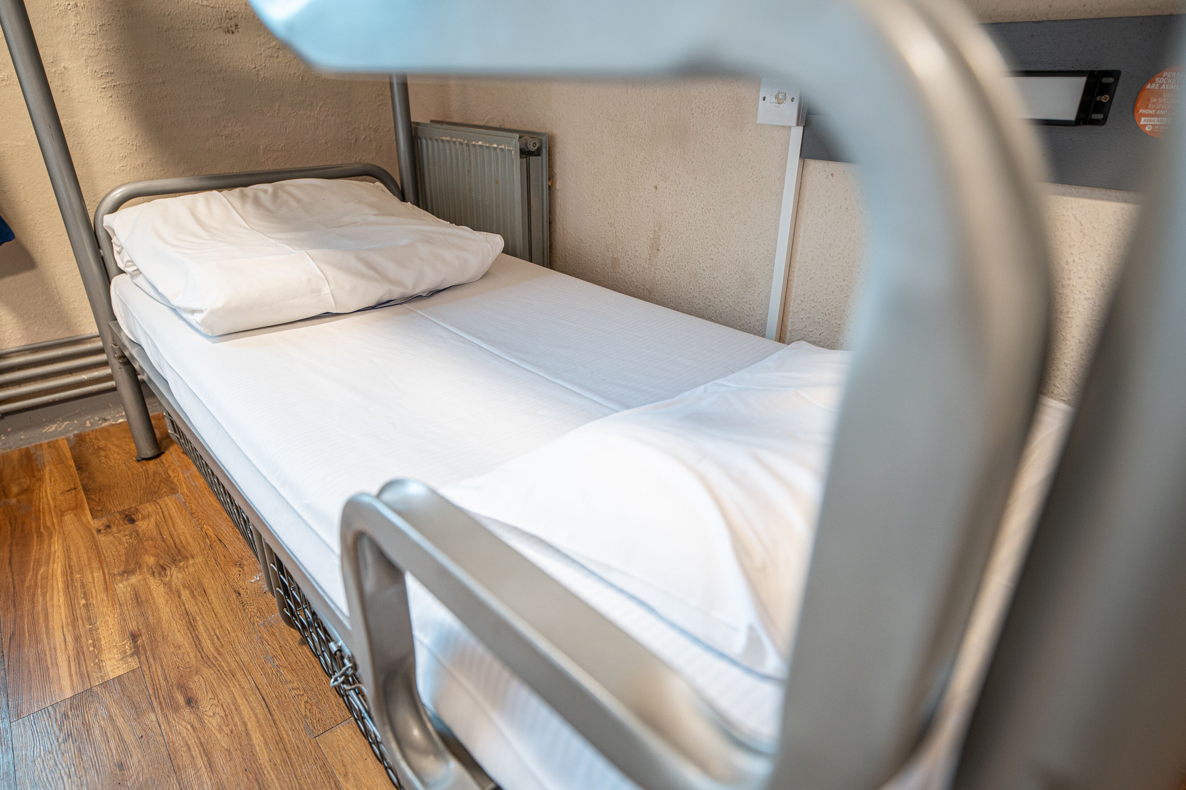 A single bed with white bedding in a room with a wooden floor and a metal headboard.