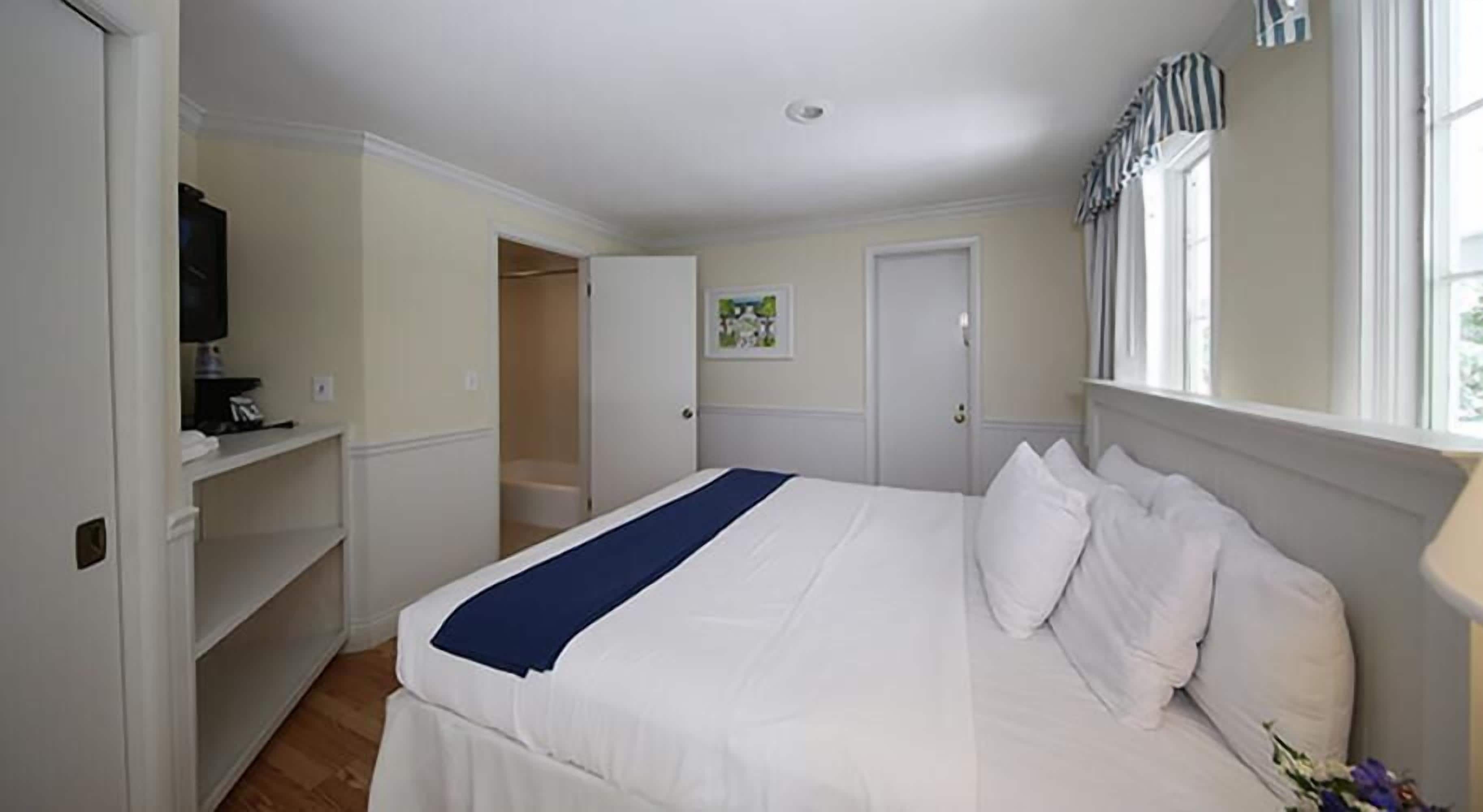 Un dormitorio con cama, armario, televisor y ventana con cortinas.