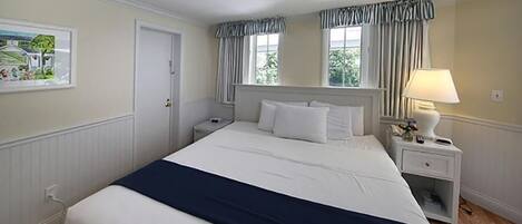 Camera d'albergo ordinata con un letto grande, un comodino con una lampada e una finestra con tende.