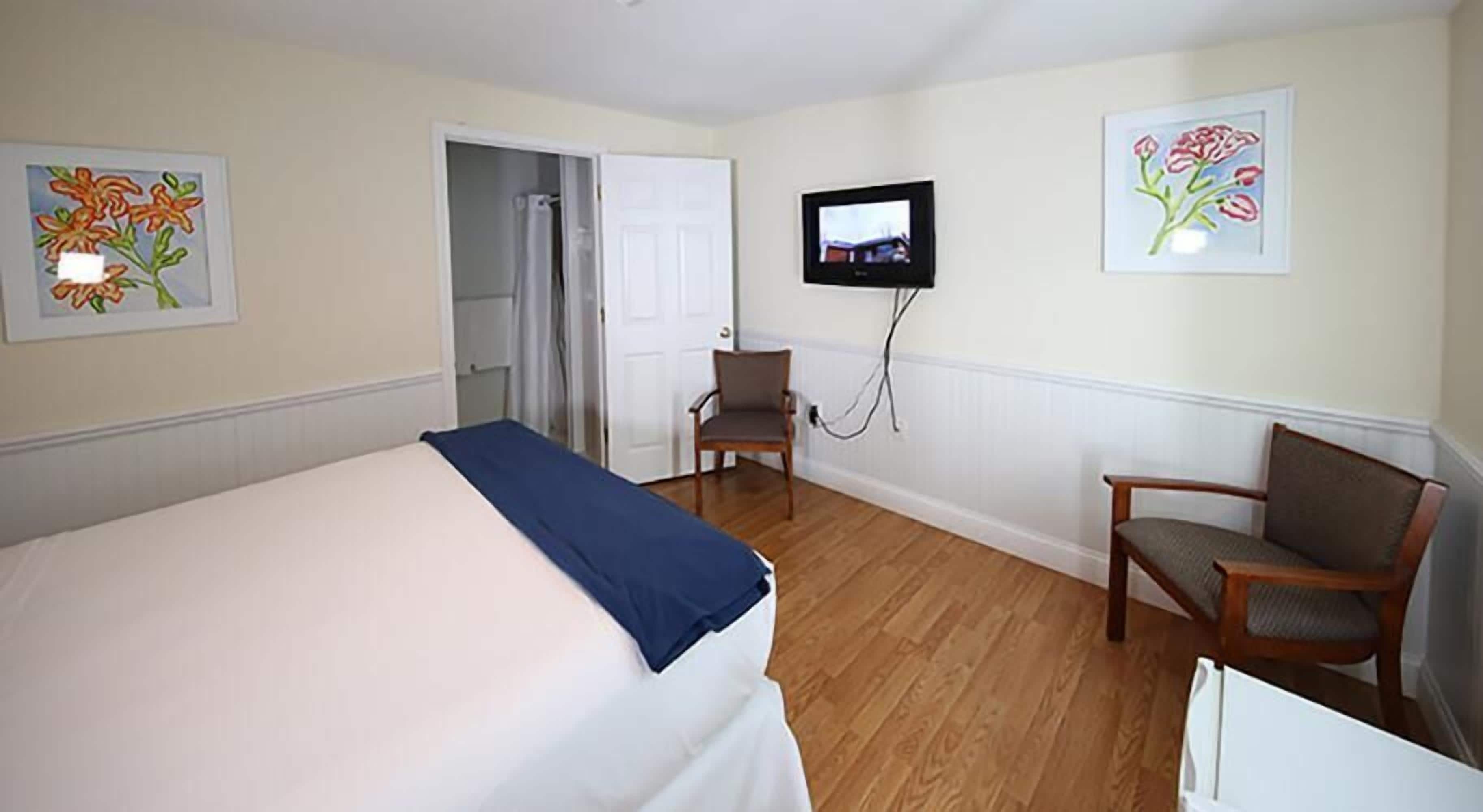 A hotel room with a bed, two chairs, a television, and artwork on the walls.