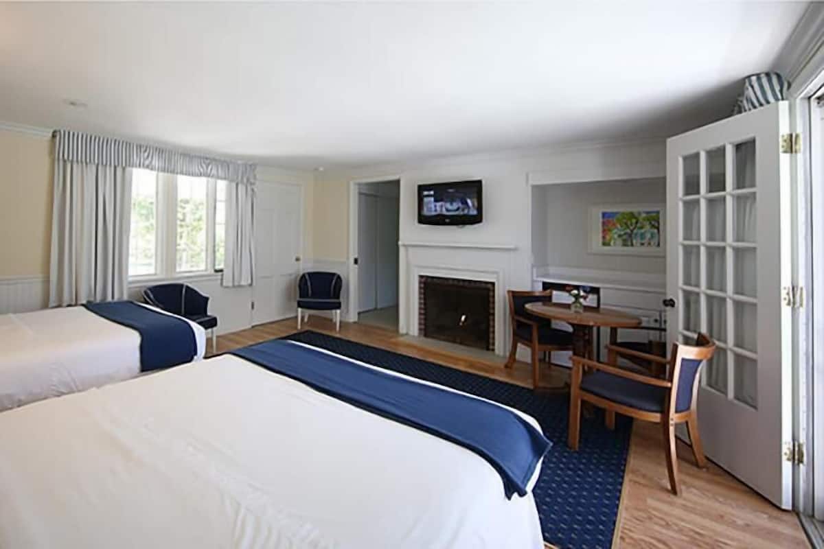 A hotel room with two beds, a TV, a fireplace, and a dining area.