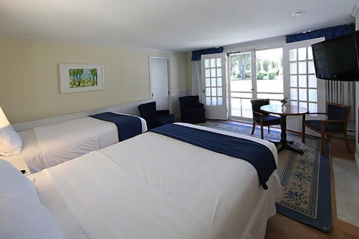 A hotel room with two beds, a desk, a chair, a television, and a window with a view of the outdoors.
