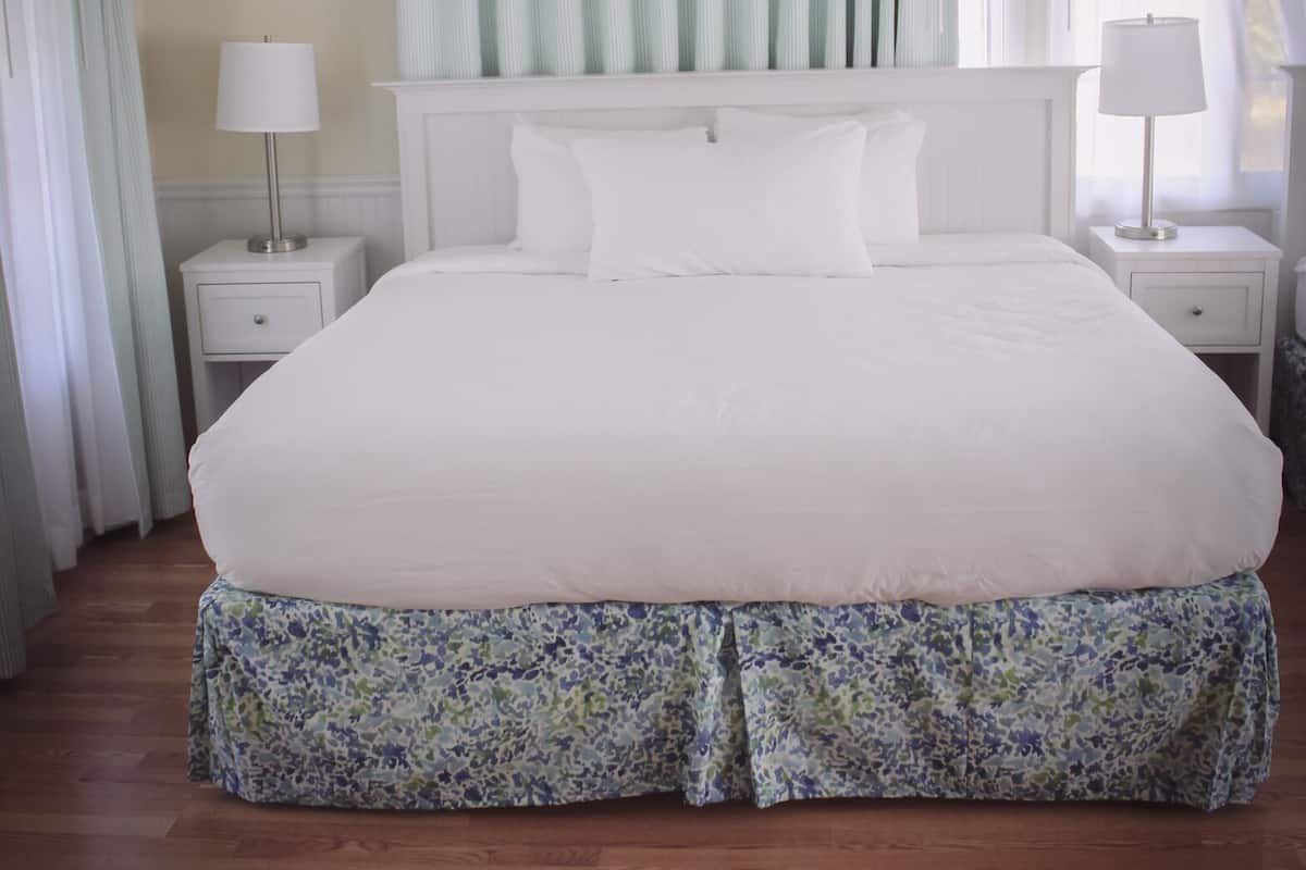 A neatly arranged bedroom with a large bed, two bedside tables with lamps, a window with sheer curtains, and a floral-patterned headboard.