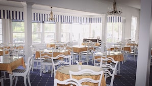 A dining area with white chairs and tables, striped window valances, and a chandelier. - Colonial Inn in Harbor Springs (Harbor Springs)