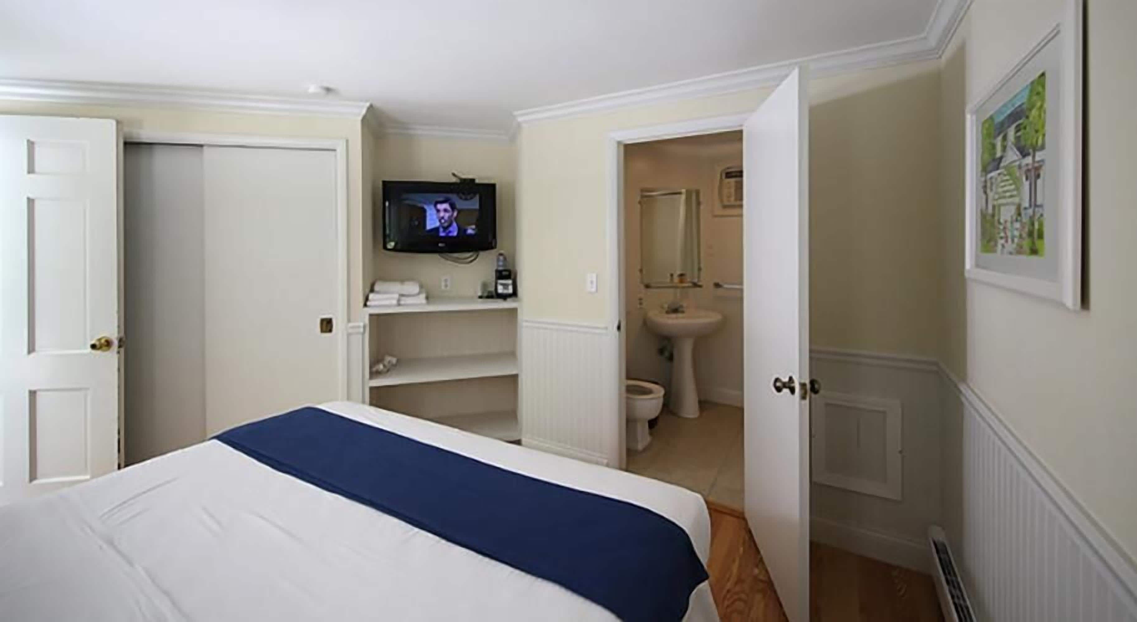 A hotel room with a bed, a television, a bathroom with a sink and toilet, and a door leading to another room.