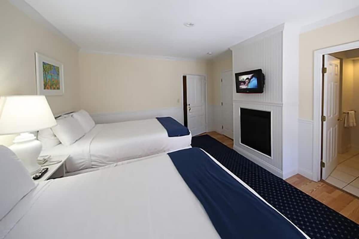 A hotel room with two beds, a TV, a desk with a lamp, and a bathroom visible through an open door.