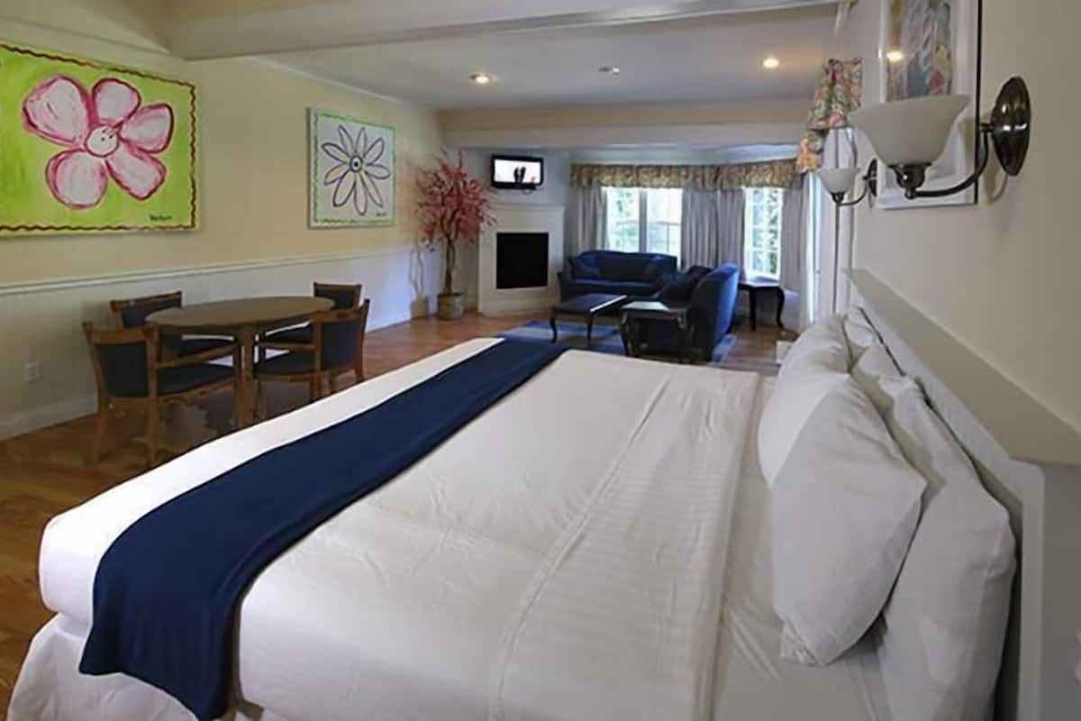 A hotel room with a large bed, a dining table, and chairs, a fireplace, and a television.