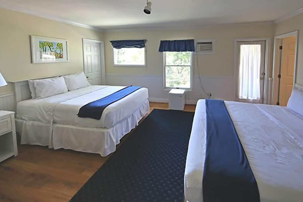 A hotel room with two beds, a nightstand, a window with curtains, and a door.