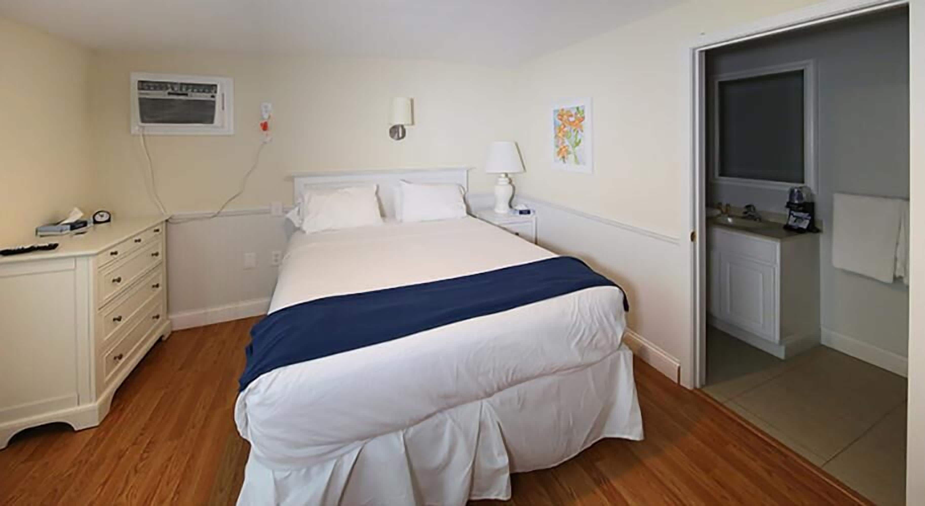 Een slaapkamer met een bed, een dressoir, een nachtkastje en een deur naar een badkamer.