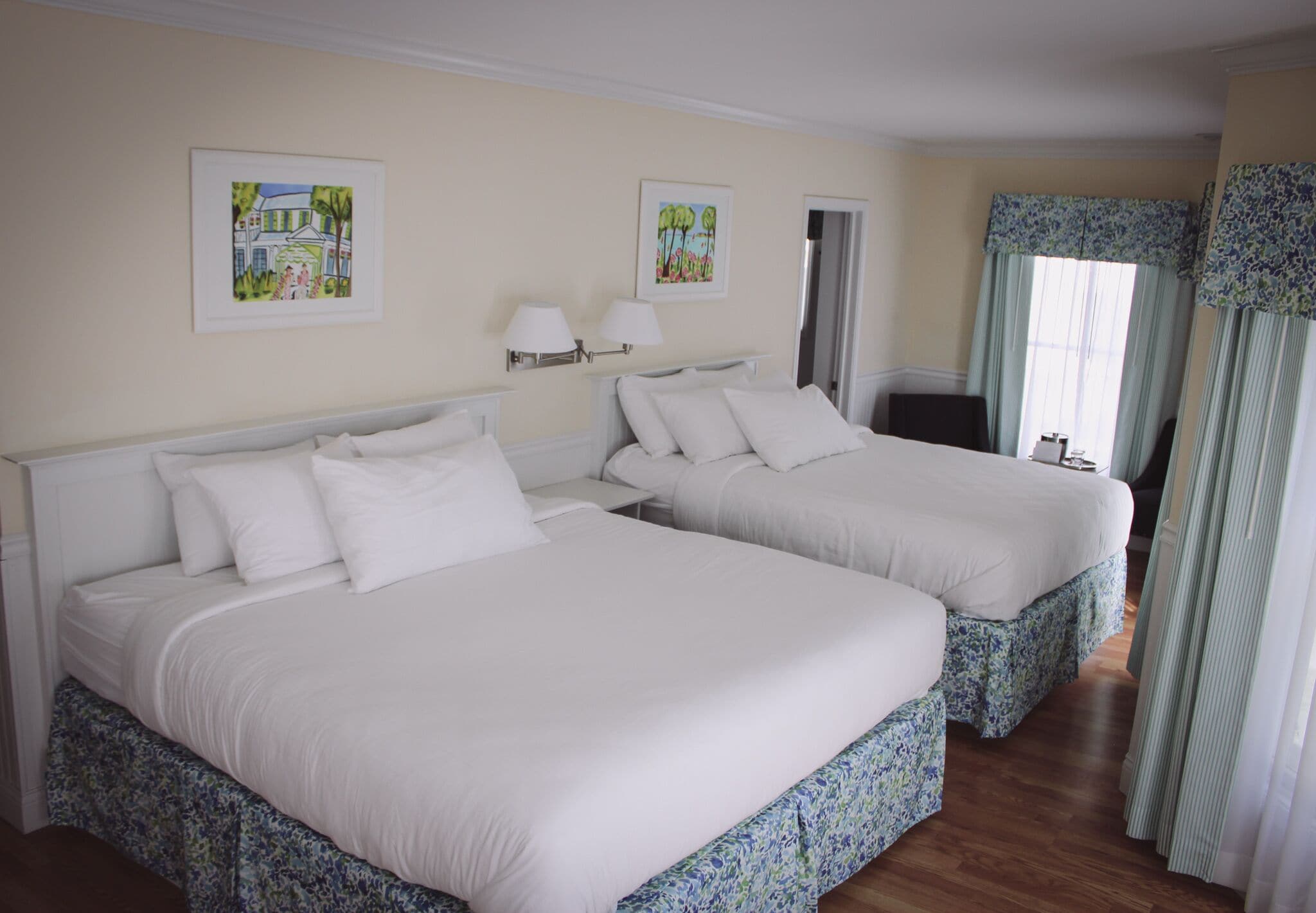 Habitación de hotel con dos camas, una ventana con cortinas y obras de arte en las paredes.