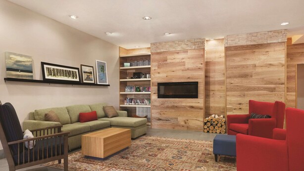 A modern living room with a sectional sofa, red armchairs, a wooden accent wall, a fireplace, and a mounted TV. - Country Inn & Suites by Radisson, Newnan, GA (Newnan)