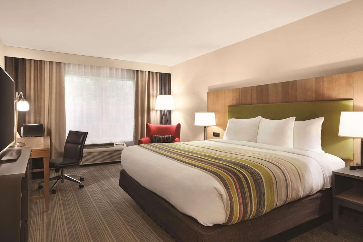 A hotel room with a large bed, a desk with a chair, a TV, and two lamps.
