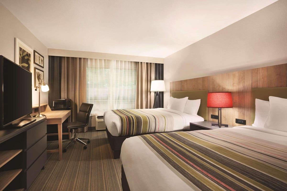 A hotel room with two beds, a desk with a computer, a television, and a lamp.