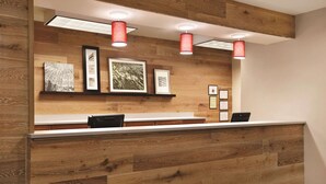 A reception desk with a wooden panel design, framed artwork on the wall, and red pendant lighting. - Country Inn & Suites by Radisson, Newnan, GA (Newnan)