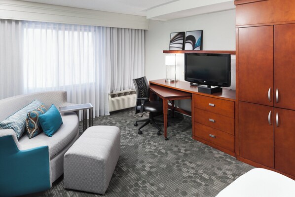 Habitación de hotel con sofá, reposapiés, escritorio, televisor y armario.