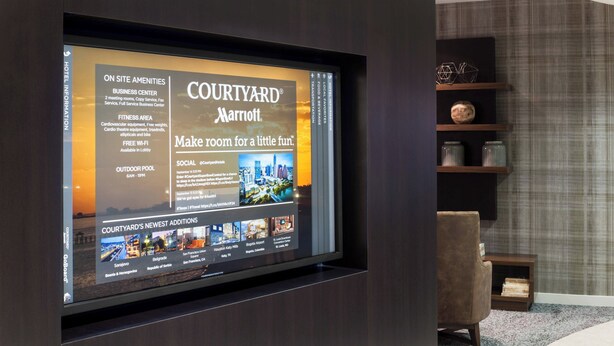 Pantalla digital en el vestíbulo de un hotel publicitando los servicios de Courtyard® Marriott®, que incluyen un centro de negocios, gimnasio, piscina al aire libre y nuevas incorporaciones.