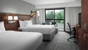 Habitación de hotel con dos camas, un escritorio, una silla y vista al exterior.