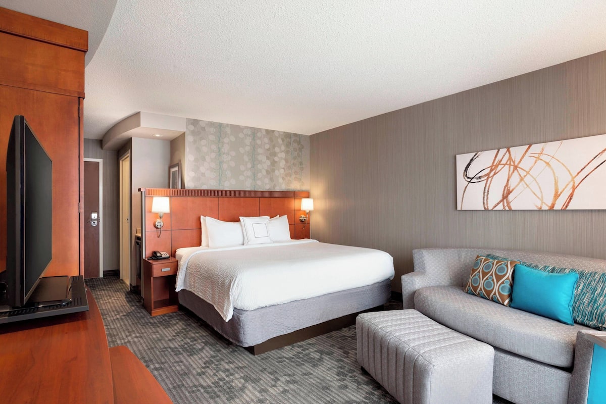 Una habitación de hotel con cama, sofá, televisión y escritorio.