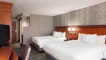 A hotel room with two beds, a desk, and a television.