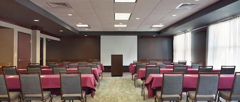 A conference room with rows of tables and chairs, a projector screen, and a carpeted floor.