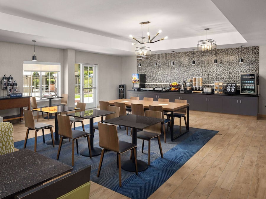 Un comedor moderno con mesas y sillas, una cocina con salpicadero decorativo, y vistas al exterior.