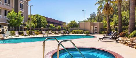 Una piscina con un pequeño jacuzzi, sillas de descanso y palmeras.