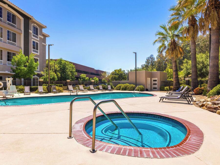 A swimming pool with a small hot tub, lounge chairs, and palm trees.