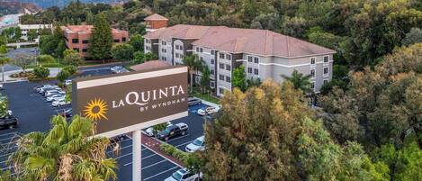 Ein Hotel namens La Quinta by Wyndham mit Parkplatz, umgeben von Bäumen und Bergen im Hintergrund.