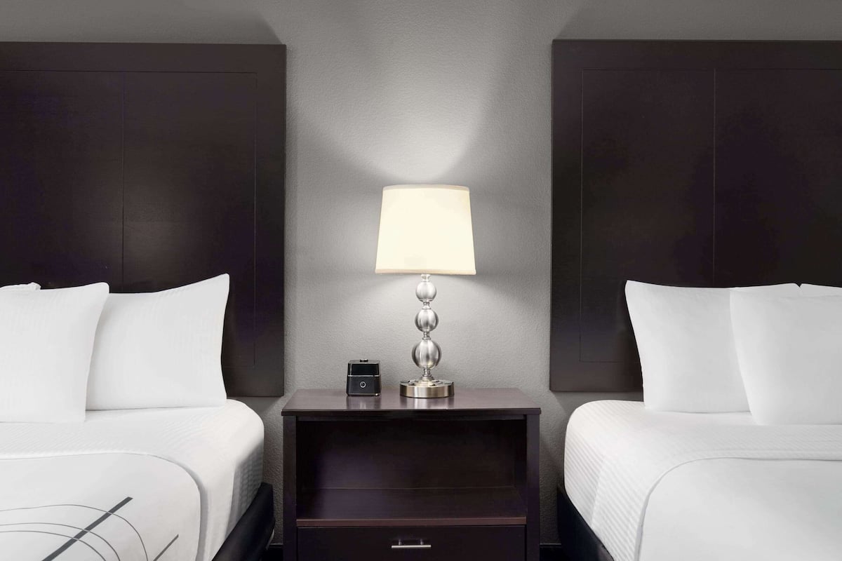 Ein Hotelzimmer mit zwei Betten, einem Nachttisch mit Lampe und einer kleinen Schublade.