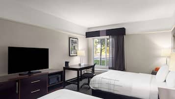 Une chambre d’hôtel avec un lit, un bureau avec un ordinateur, une télévision et une fenêtre avec des rideaux.