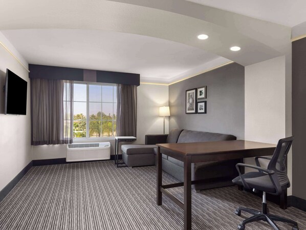 A hotel room with a bed, a desk, a chair, a lamp, and a TV.