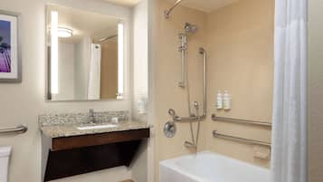 A modern bathroom with a bathtub, a sink with a granite countertop, a mirror, and a shower with a grab bar.