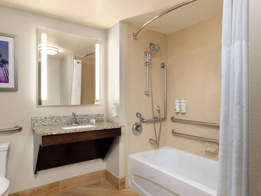 A modern bathroom with a bathtub, a sink with a granite countertop, a mirror, and a shower with a grab bar.