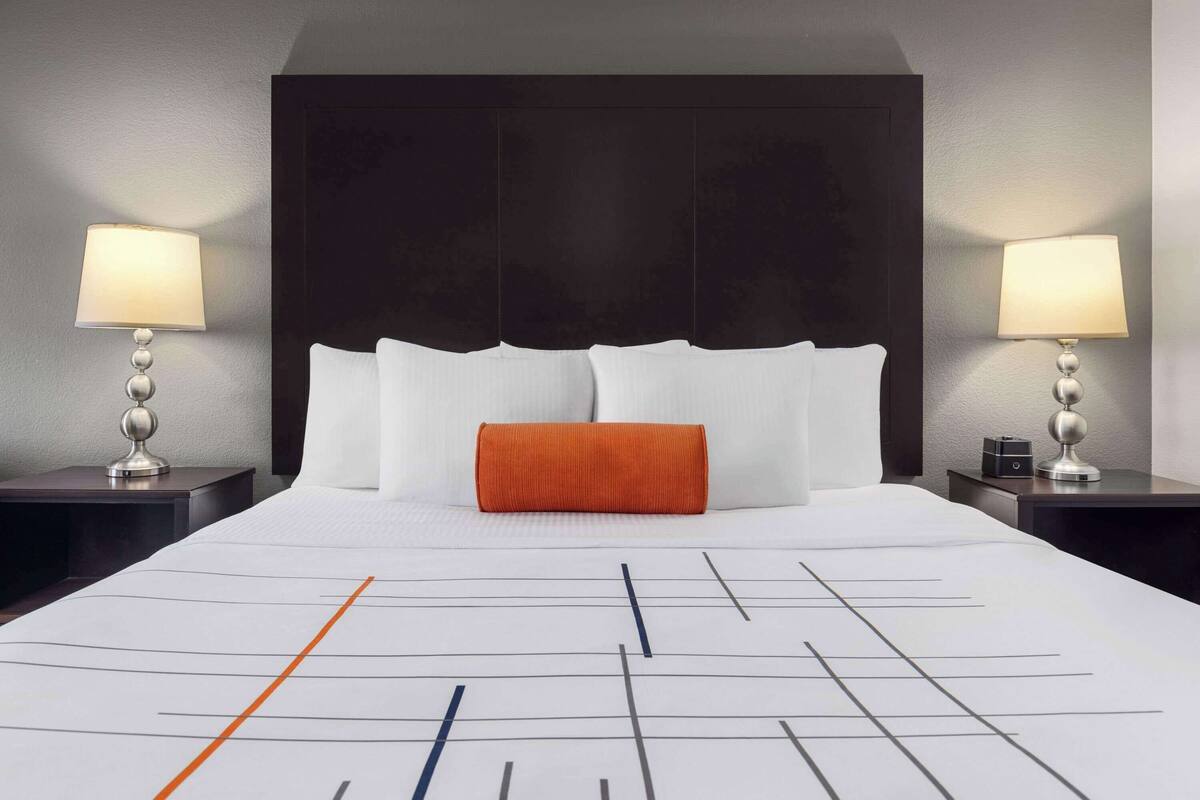 Ein Hotelzimmer mit einem großen Bett, zwei Nachttischen mit Lampen, einem dunklen Kopfteil und einer gemusterten Bettdecke.