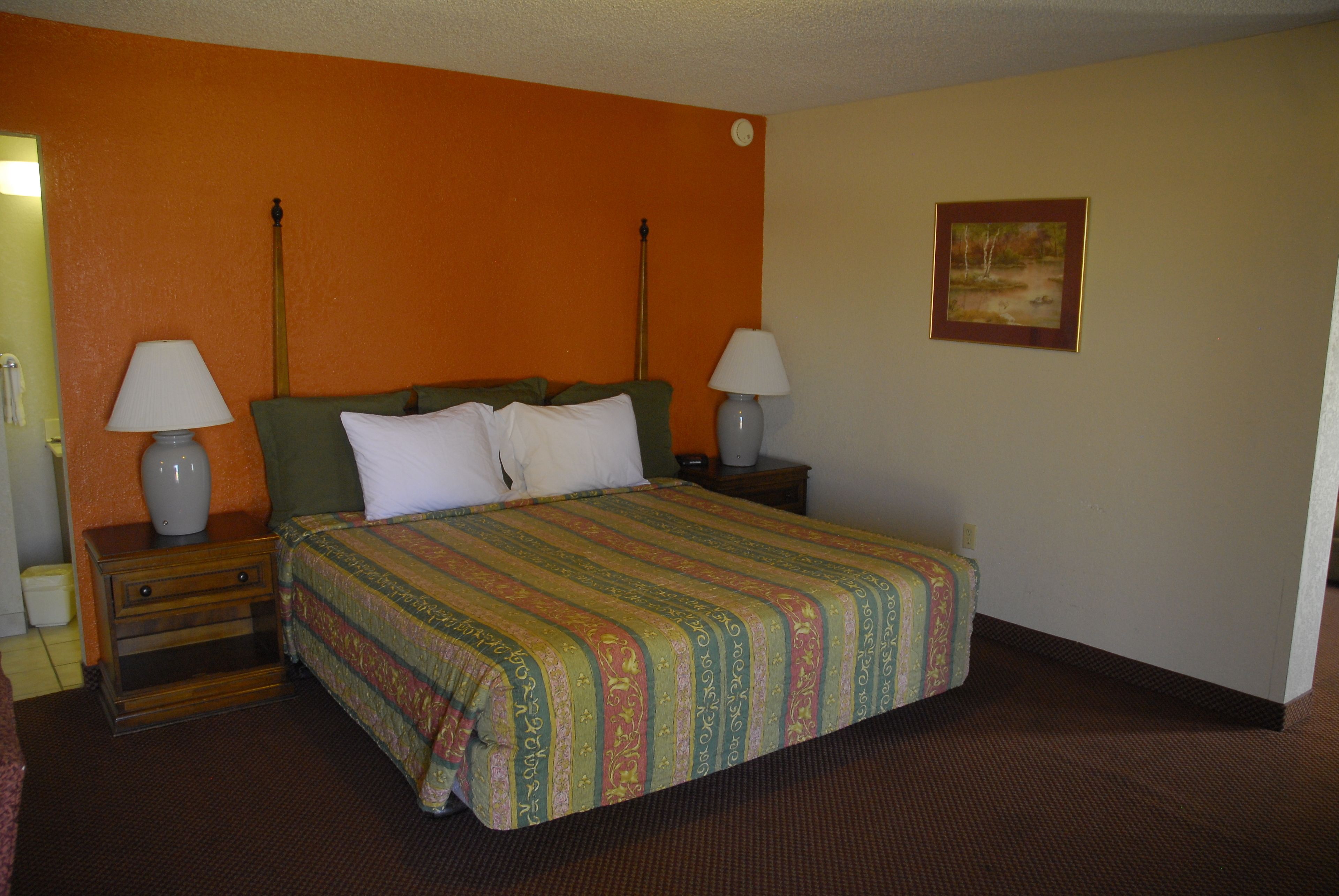 A hotel room with a large bed, two bedside tables with lamps, a nightstand, and a framed picture on the wall.