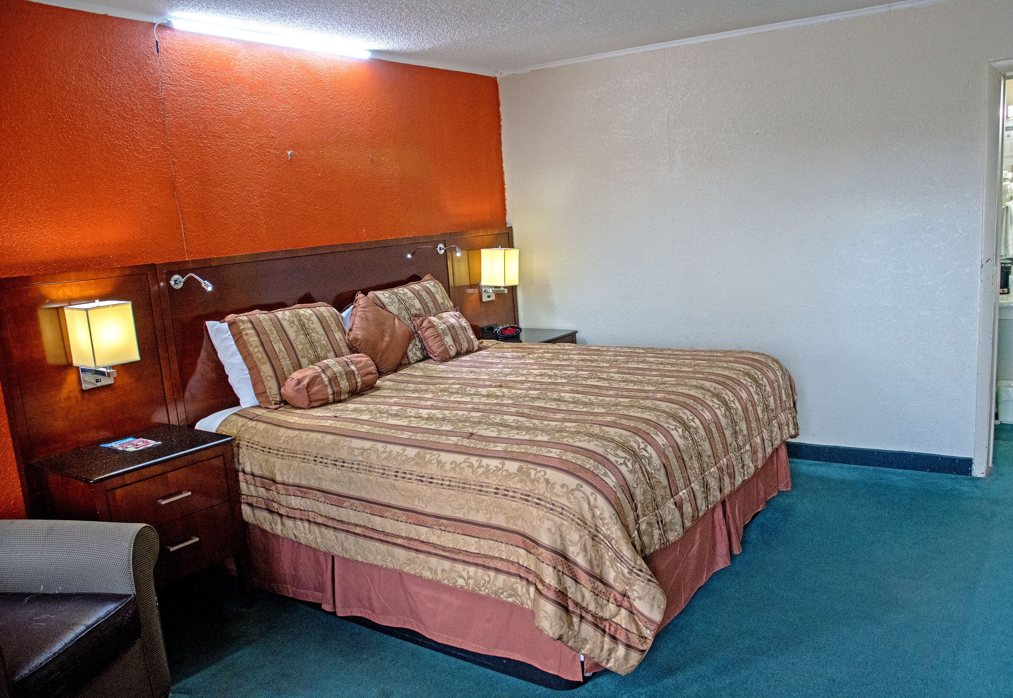 A hotel room with a large bed, two bedside tables with lamps, a chair, and a carpeted floor.