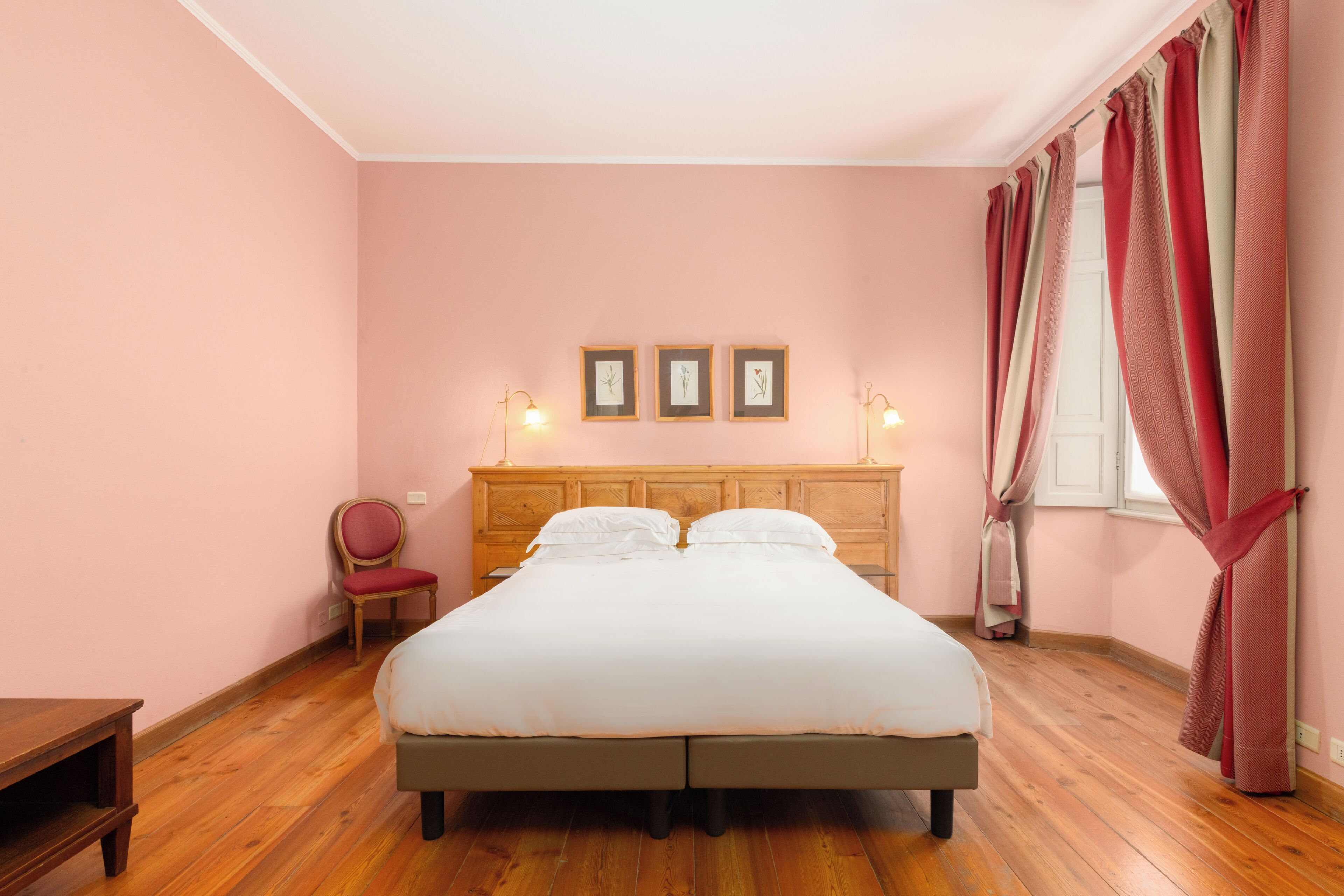 A bedroom with a wooden bed, a chair, a bedside table, and a window with curtains.