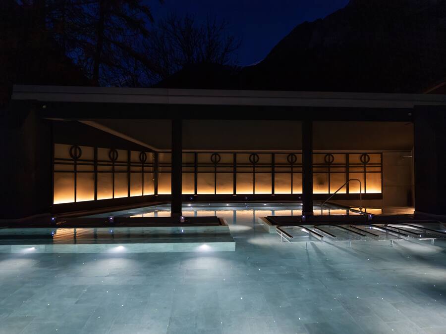 A modern building with a large pool area, illuminated by ambient lighting.