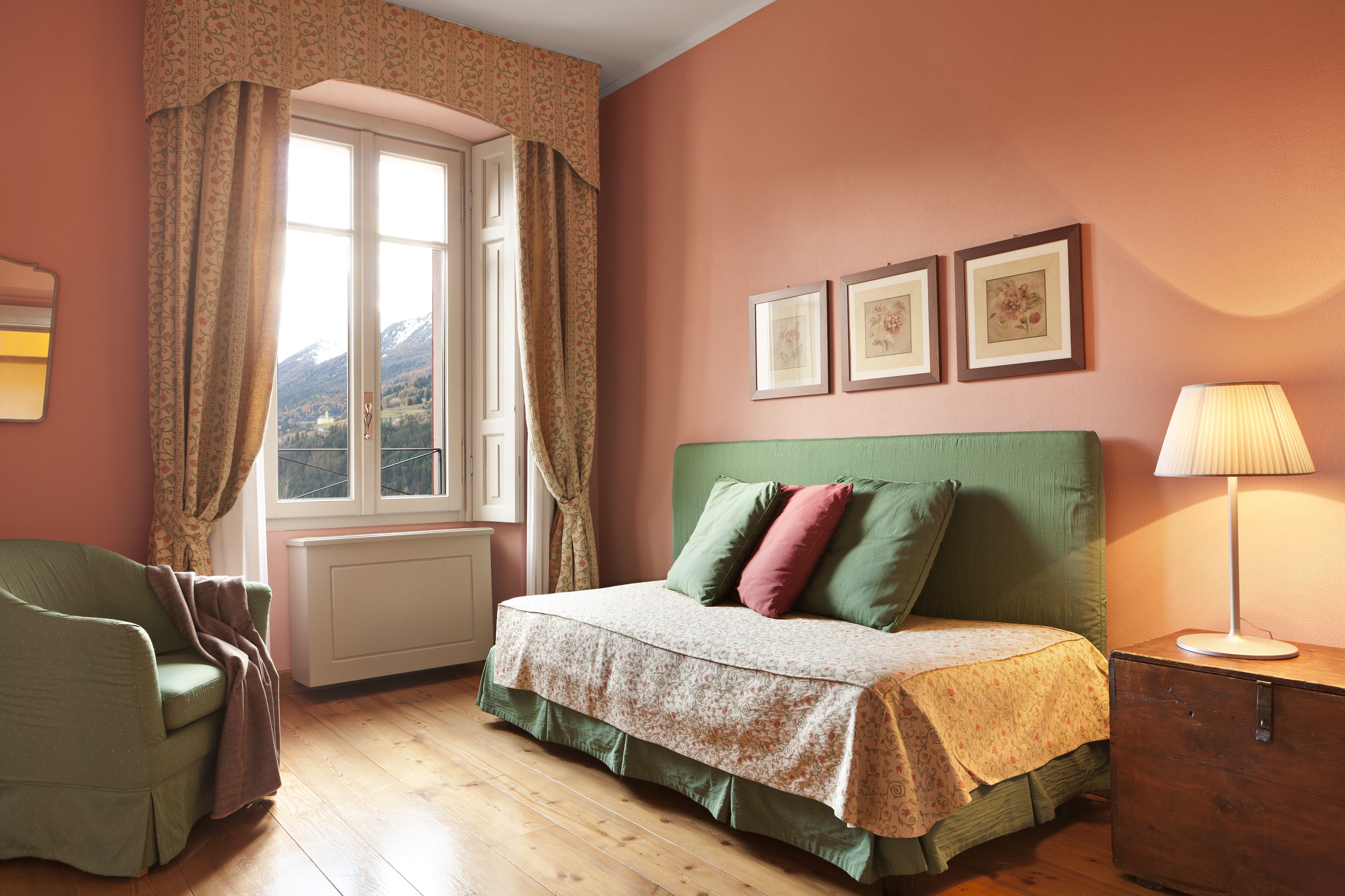 A bedroom with a bed, a chair, a window with curtains, and framed pictures on the wall.