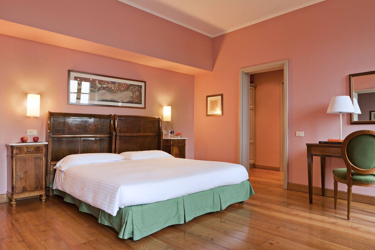 Ein Schlafzimmer mit einem hölzernen Bett, einem grünen Bettüberzug, zwei Nachttischen, einem Beistelltisch, einem Stuhl und einem Bild an der Wand.