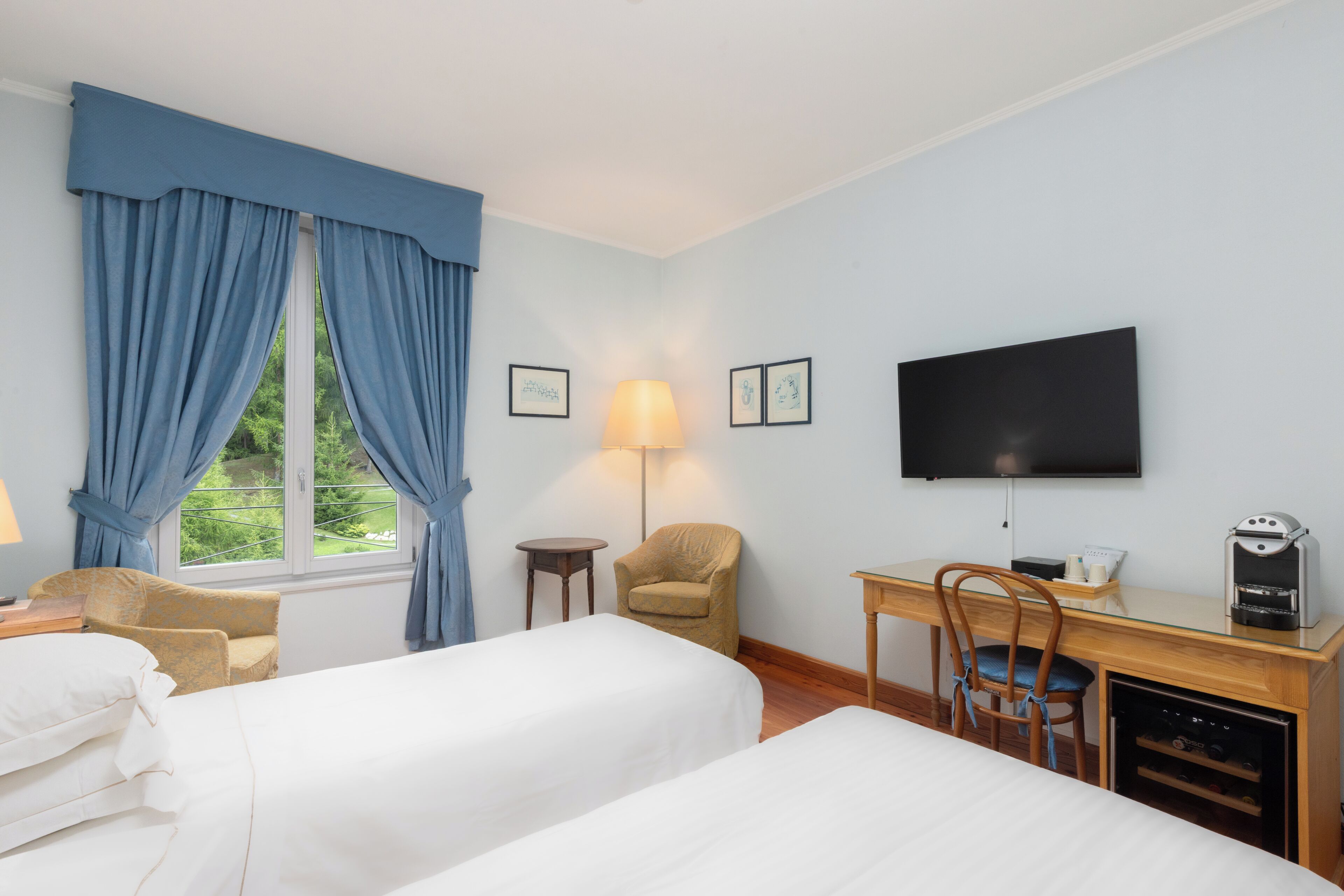 Una camera d'albergo con due letti, una scrivania con una macchina del caffè, una televisione e una finestra con tende.