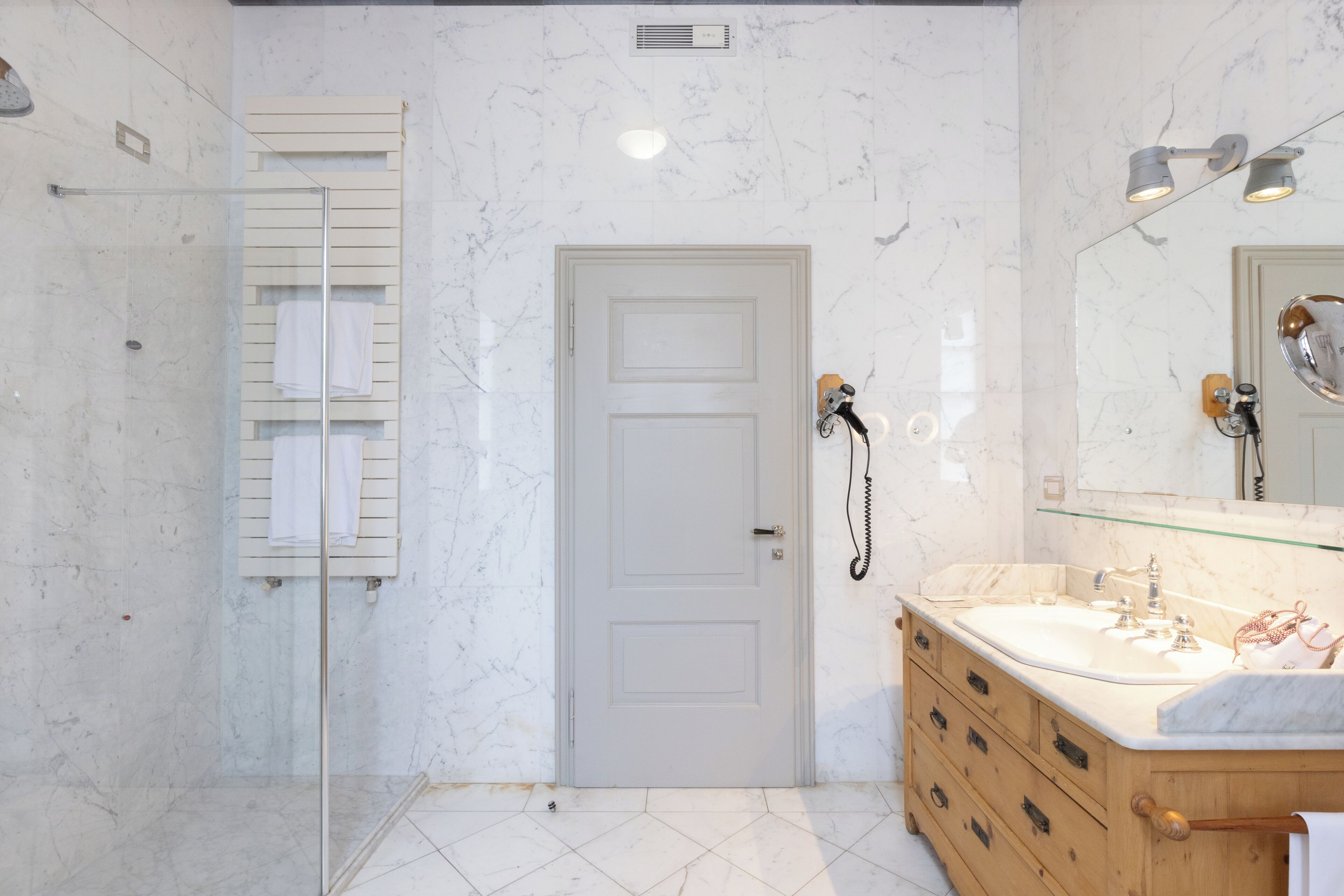 Un baño con cabina de ducha de vidrio, una puerta blanca, tocador con espejo y un perchero para toallas.